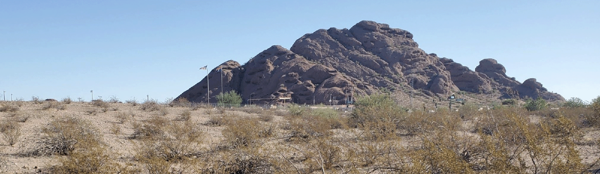 Panoramic photo of red rock formations at Papago Park Military Reservation, rising behind a desert landscape dotted with low shrubs