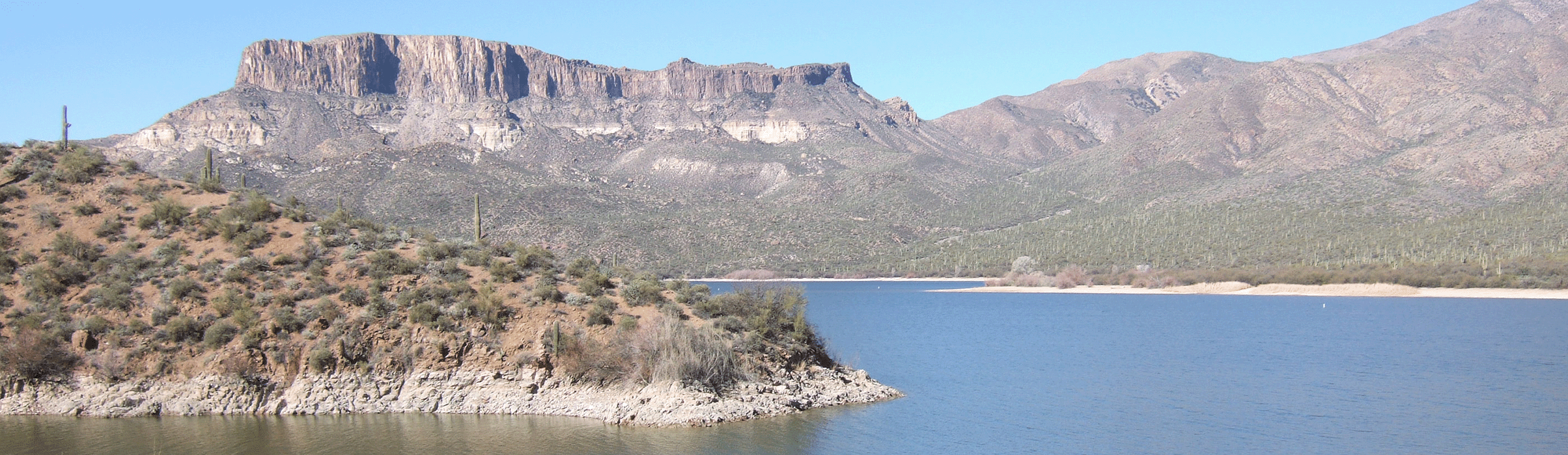 Panoramic photo of a desert lake surrounded by rocky hills, saguaro cacti, and flat-topped mountains at Luke Waterdog Recreation Annex 