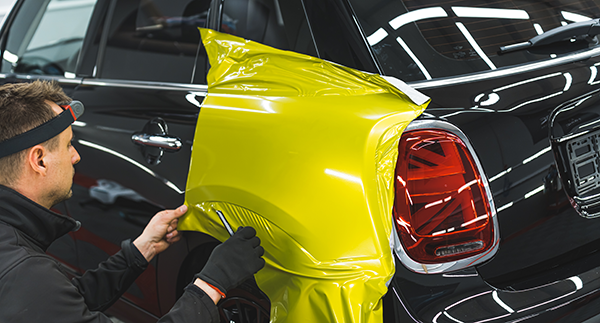 Technician applying a vinyl wrap to a car&rsquo;s rear side panel.